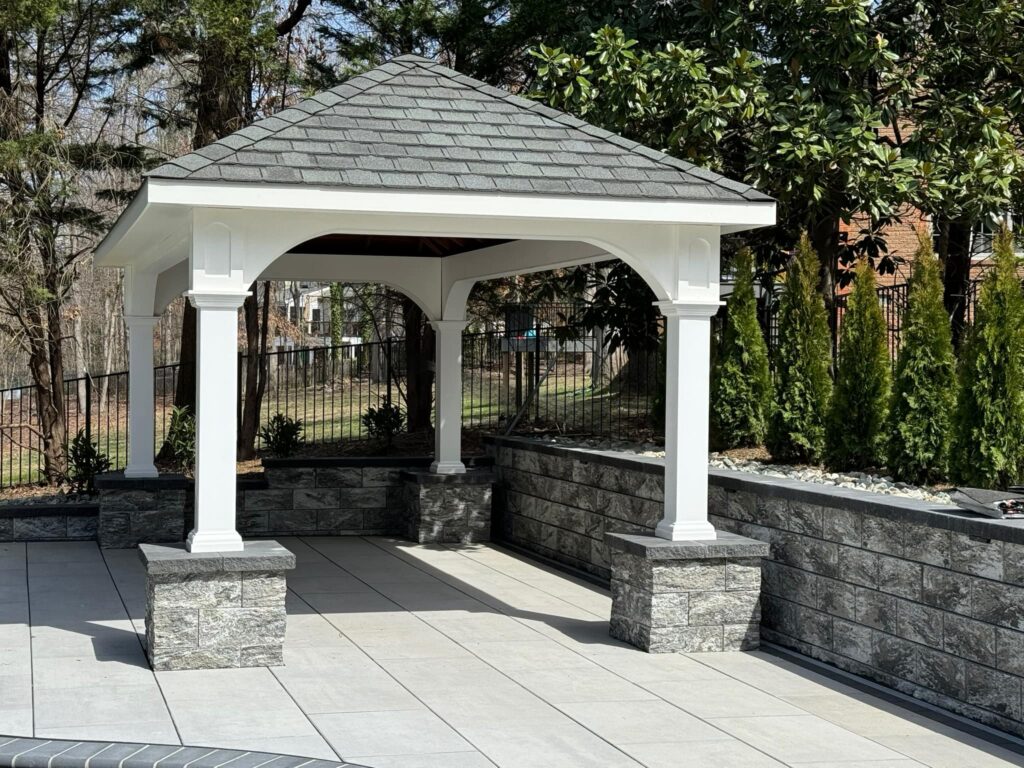 Backyard pavilion featuring white columns and stone base on a paver patio in Virginia.