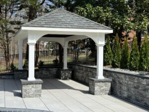 Backyard pavilion featuring white columns and stone base on a paver patio in Virginia.