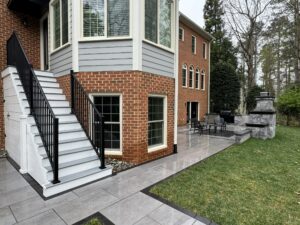 Brick home with elevated composite deck, staircase, and gray paver patio below in Virginia