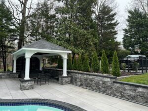 White backyard pavilion overlooking a pool with light gray paver deck in Virginia
